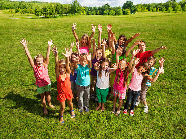 Hier spielen unsere SchülerInnen in der Naturparkwiese. Alle Kinder haben die Hände in der Luft und rufen yeaa in die Kamera Hier sieht man wie unsere SchülerInnen in der Wiese stehen und sich auf den nächsten spannenden Programmpunkt in der Natur freuen.