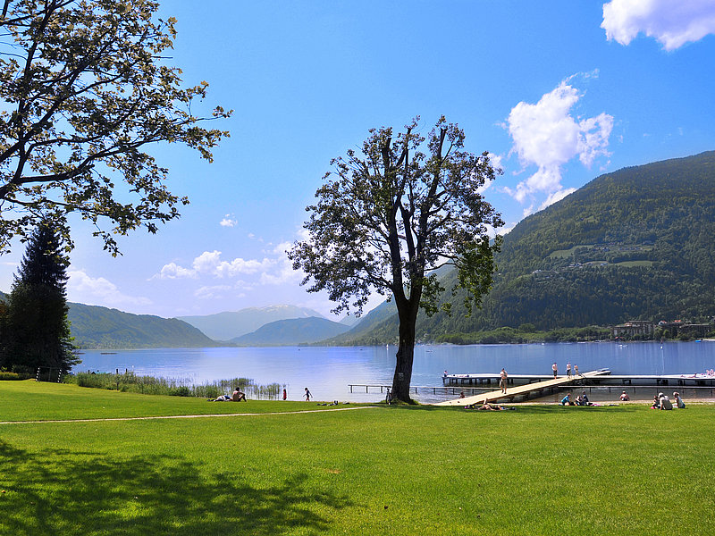 Der Ossiacher See ist ein wahres Naturerlebnis. Hier hat man beim Sportanbieter Blasge direkten Seezugang. Wer kann einem solchen Panorama widerstehen Das Foto zeigt den direktion Seezugang direkt neben dem Sport- und Programmanbieter Blasge am Ossiacher See. Auf dem Steg ins ruhige Wasser des Ossiacher Sees tummeln sich schon frühmorgens die ersten Badebegeisterten. auch auf der Liegewiese im Vordergrund sieht man schon einige Badegäste. Hier können sich unsere SchülerInnen so richtig austoben.