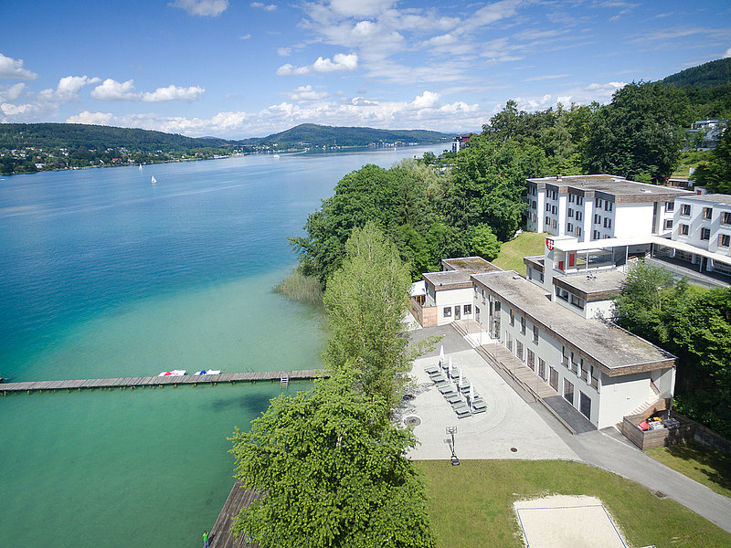 Das Sonnencamp Sekirn befindet sich direkt am Südufer des Wörthersees. Das Ferienhaus hat direkten Seezugang. die großzügige Freizeitanlage verfügt über einen großen eigenen Strand mit mehreren Steganlagen und zahlreichen Sportmöglichkeiten Das Foto zeigt das Ferienhaus Sonnencamp Sekirn aus der Vogelperspektive. Links im Bild einer der Stege mit direktem Seezugang zum Wörthersee und die Liegewiese